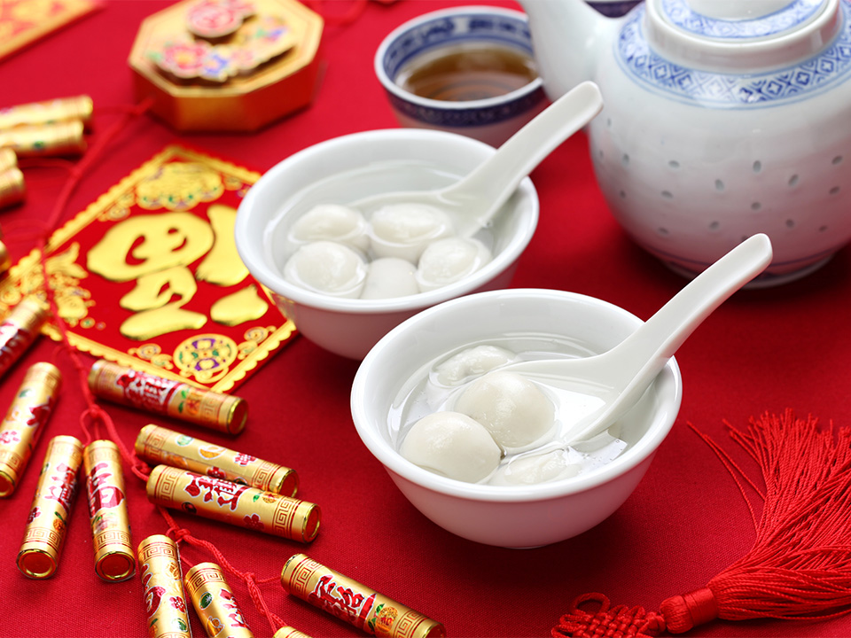 两碗汤圆放在红桌上，旁边有各种传统新年装饰。